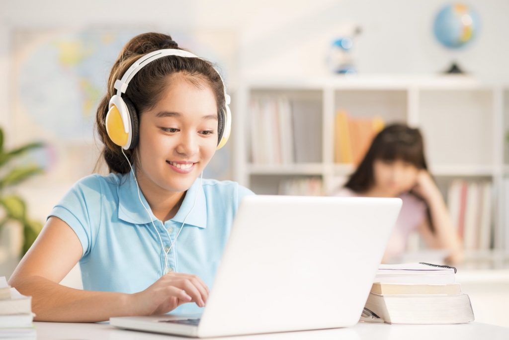Vietnamese schoolgirl with headphones using laptop in the class