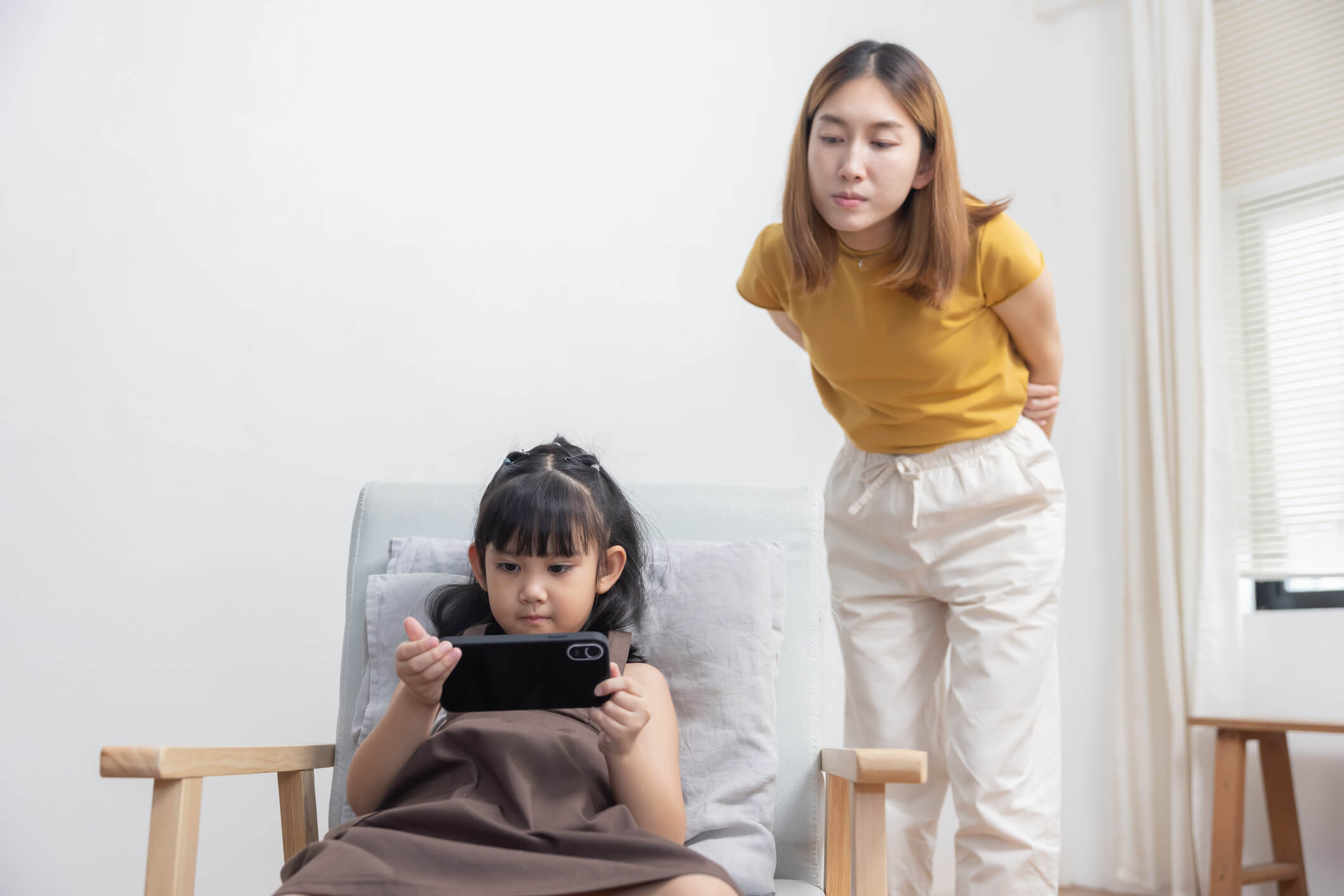 Worried Mother Looking at Her Kid Playing Game on the Smartphone