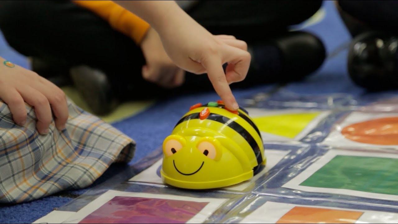 Close-up of a child's hand pressing buttons on a Bee-Bot educational robot.