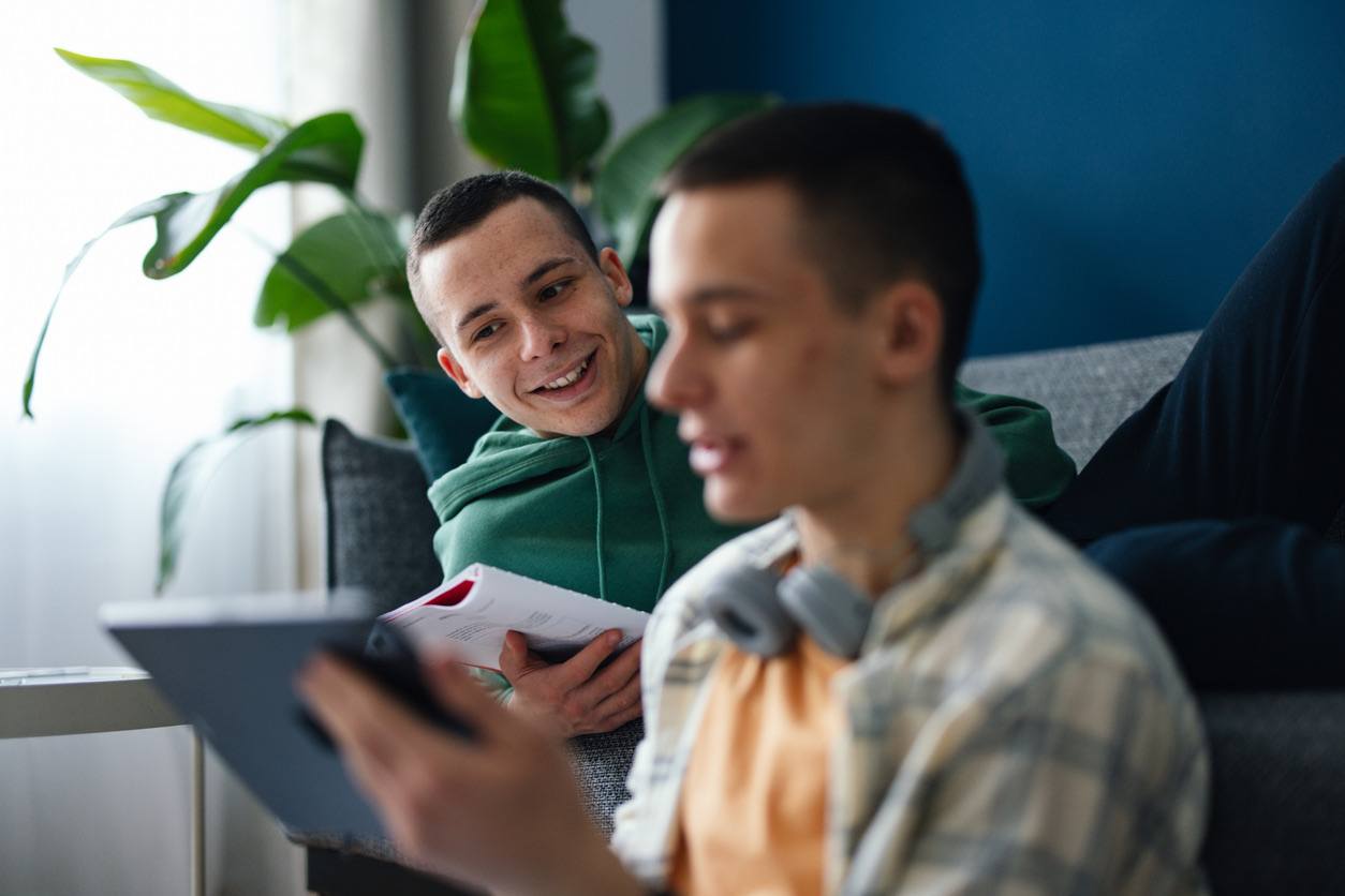 Two young men studying together at home, one using a tablet.