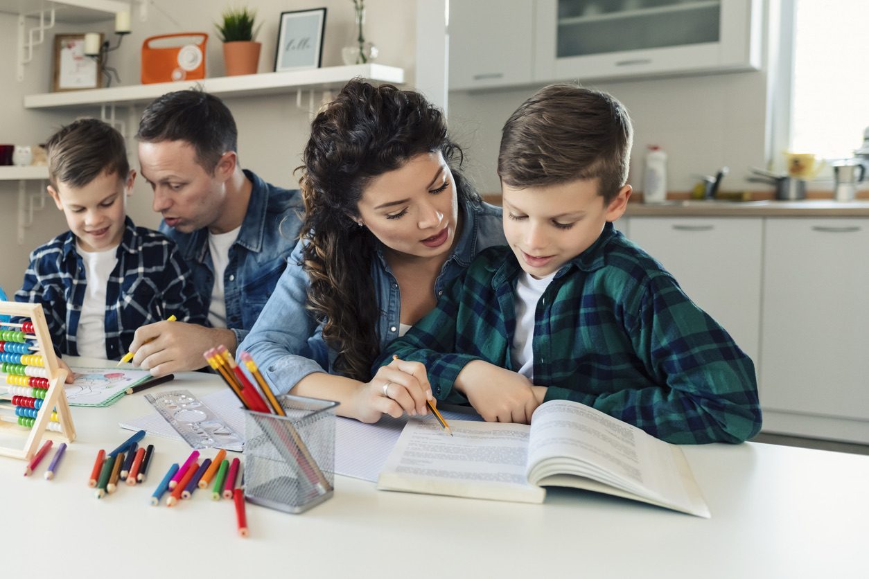 Parents helping their two sons with homework at the kitchen table.