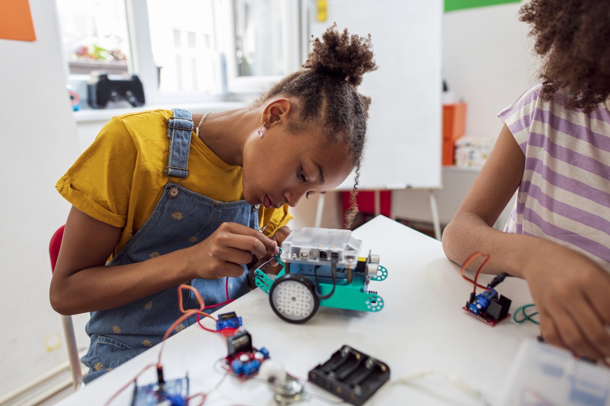 Young girl focused on assembling a small robotic project at a table.