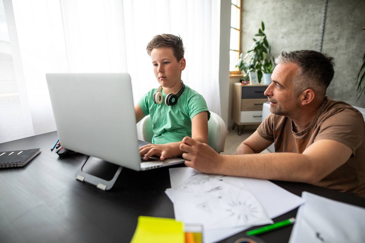 Father and son working together on a laptop at home, focused on the screen.