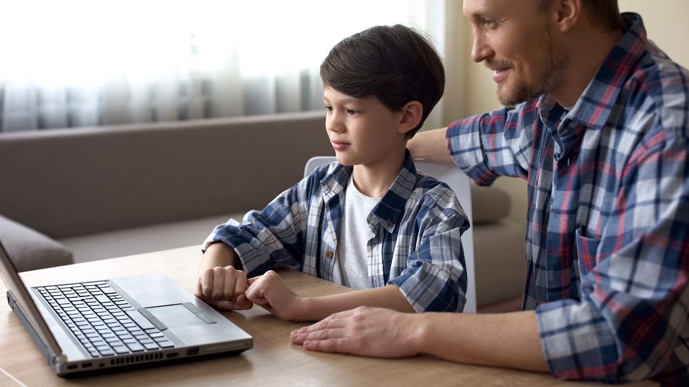 Father and young son using a laptop together, both smiling and engaged.