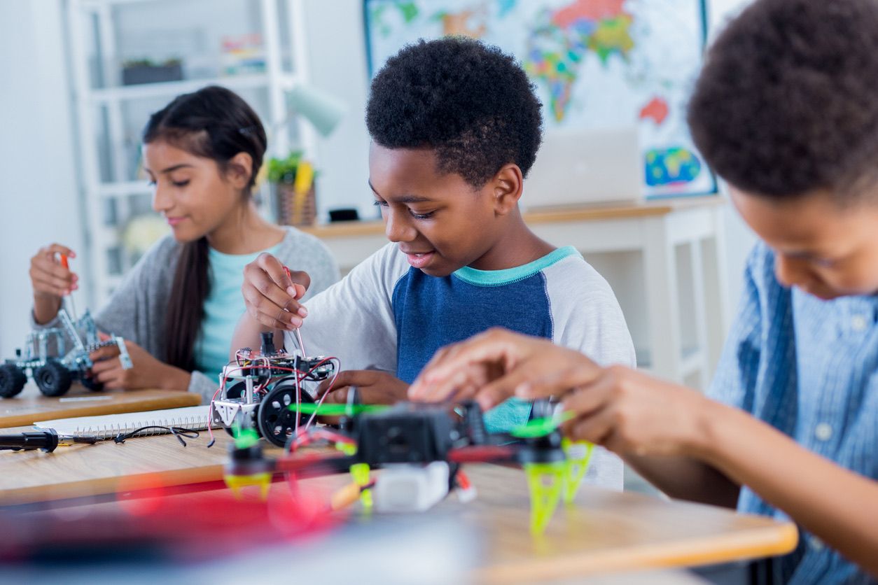 Three children working on robotics projects in a classroom.