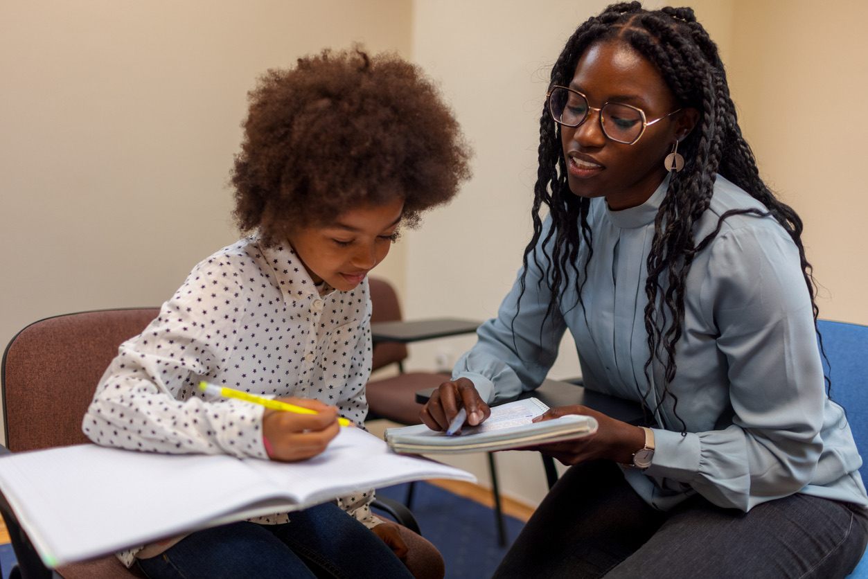 Young girl with dark skin studying with a mentor in a classroom.