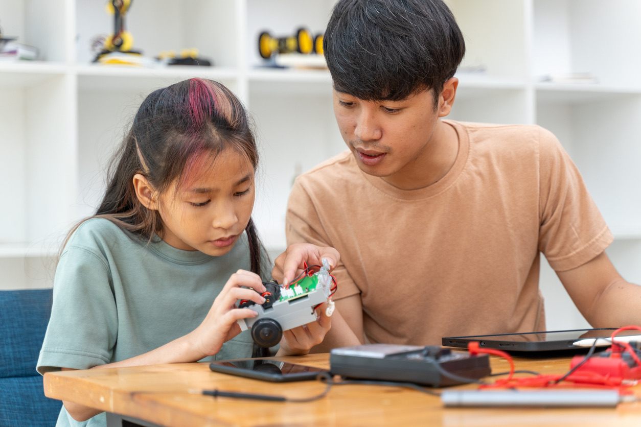 Mentor helping young girl assemble a robot