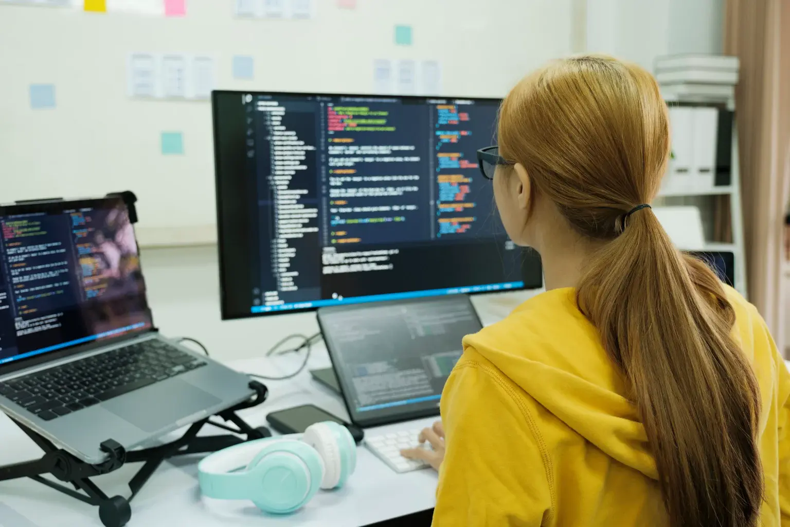 A student writing code across a laptop and a monitor